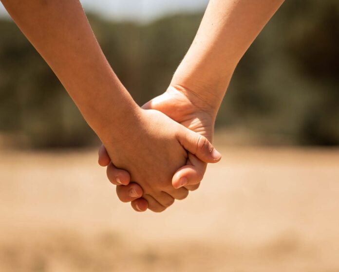 Beautiful closeup shot of a couple holding hands on a blurred background of a field